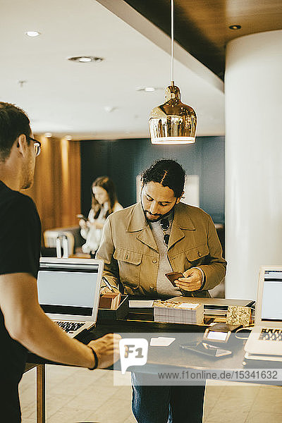 Man looking at tourist signing at reception desk in hotel