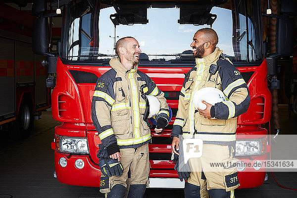 Happy firefighters talking while standing in front of fire engine at fire station