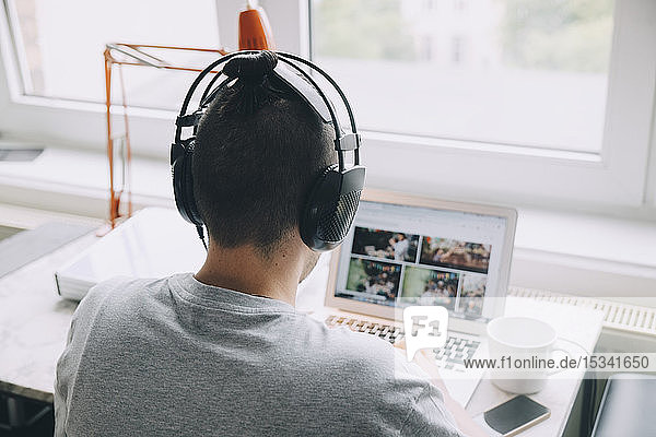 Rückansicht eines kreativen Geschäftsmannes mit Kopfhörern und Laptop am Schreibtisch im Büro