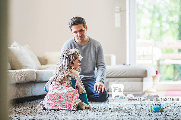 Father looking at daughter kneeling on carpet at home