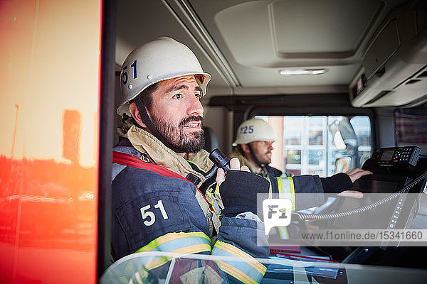 Mittlerer erwachsener Feuerwehrmann spricht am Mikrofon  während er mit seinem Kollegen im Feuerwehrauto sitzt
