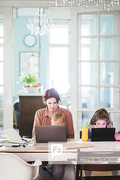 Woman working on laptop while sitting with children at table