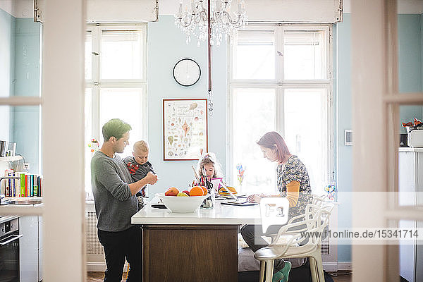 Father playing with son while standing by girl and woman busy at kitchen island