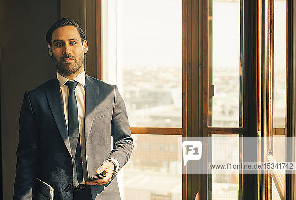 Portrait of confident male advisor standing by window at legal office