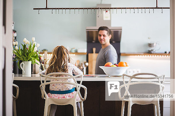 Vater sieht Tochter beim Lernen an  während er in der Küche sitzt
