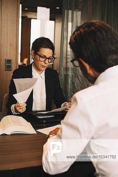 Weibliche Finanzberaterin prüft Dokumente  während sie mit dem Kunden in einer Besprechung im Büro sitzt