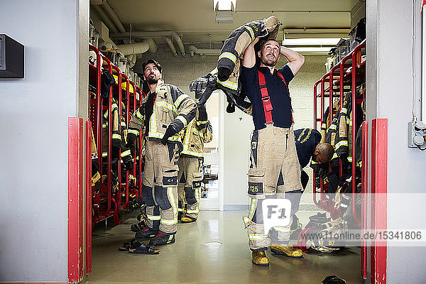 Feuerwehrleute tragen Arbeitsschutzkleidung in der Umkleidekabine  während sie zur Feuerwache aufschauen