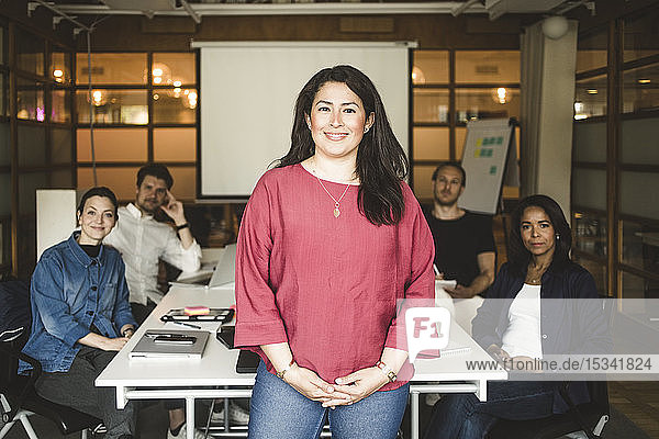 Porträt einer selbstbewussten Geschäftsfrau  die mit dem Team im Hintergrund im Sitzungssaal steht