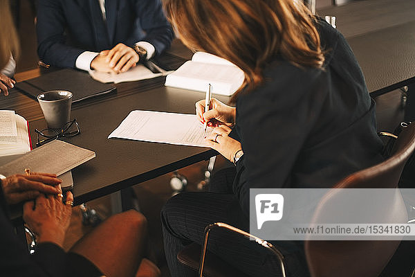 Female lawyer signing documents while sitting in meeting with colleagues at office
