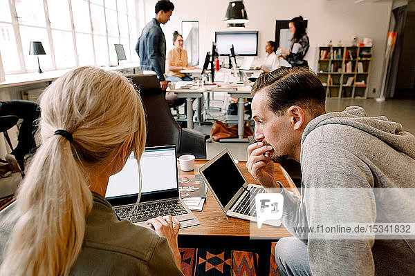 Männliche und weibliche Berufstätige  die über einen Laptop arbeiten  während sie am Bürotisch sitzen