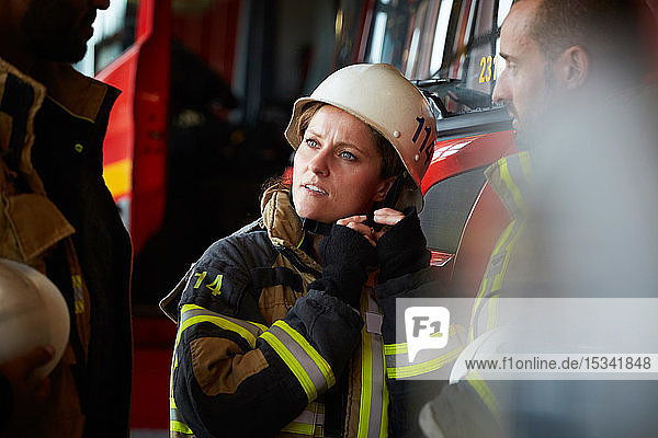 Female firefighter wearing helmet while talking with other coworkers in fire station