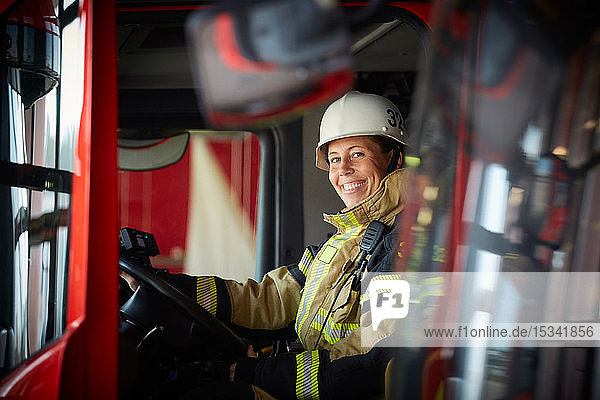 Porträt einer lächelnden Feuerwehrfrau  die im Feuerwehrauto der Feuerwache sitzt