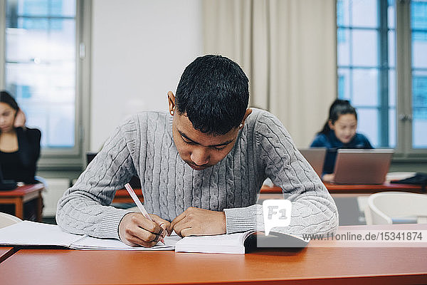 Teenager schreibt auf Buch  während er in der High School am Schreibtisch lernt
