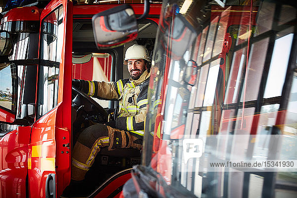 Portrait of smiling male firefighter sitting in fire truck at fire station