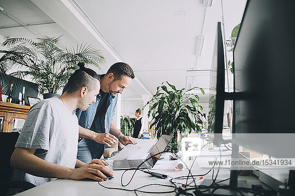 Männliche Unternehmer diskutieren über Dokument am Schreibtisch im Kreativbüro