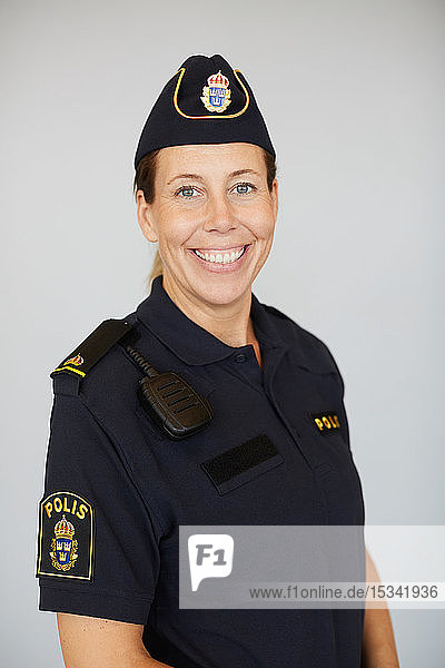 Portrait of smiling policewoman in uniform standing against white background