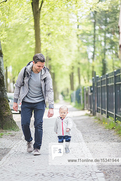 Full length of smiling father looking at son walking on footpath