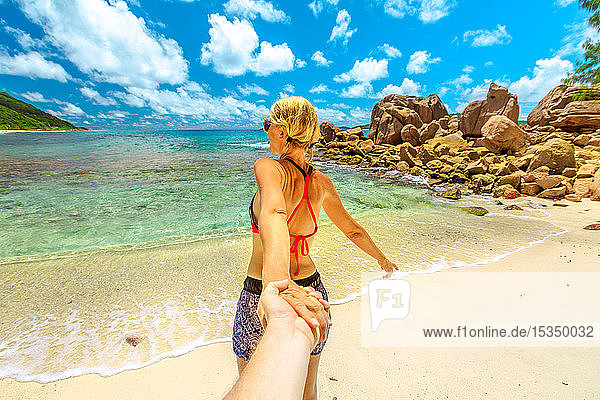 Blonde Touristin im Bikini hält die Hand ihres Partners am Anse Caiman Beach mit natürlichem Pool in La Digue  Seychellen  Indischer Ozean  Afrika