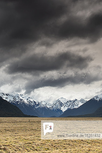Mann in rotem Mantel mit Blick auf schneebedeckte Berge  Fiordland National Park  UNESCO Weltkulturerbe  Südinsel  Neuseeland  Pazifik