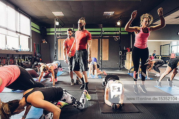 Gruppe von Frauen  die mit männlichen Trainern im Fitnessstudio trainieren und Kniebeugen machen