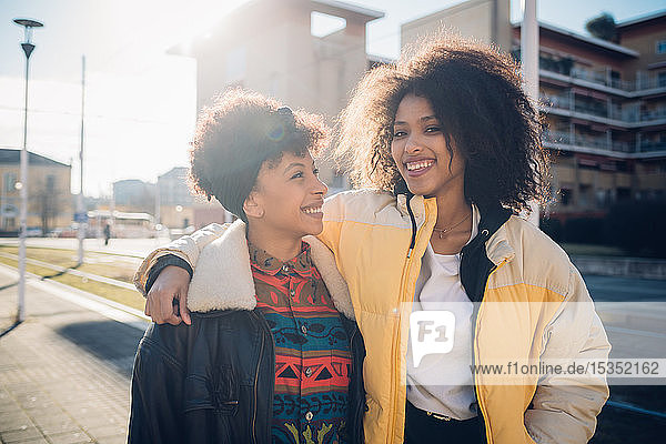 Two cool young female friends on sunlit urban sidewalk  portrait