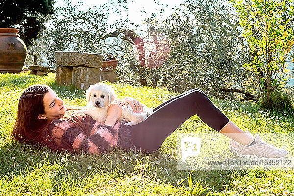 Girl lying in orchard with a cute golden retriever puppy on her stomach  Scandicci  Tuscany  Italy