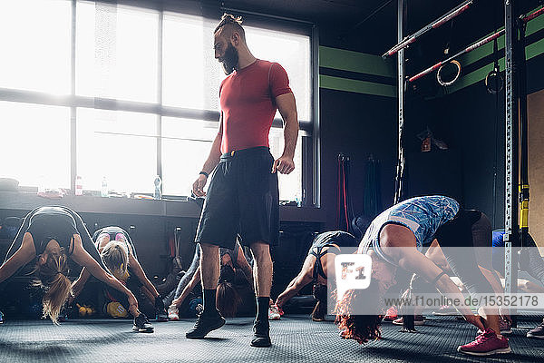 Frauen trainieren in Turnhalle mit männlichem Trainer  beugen sich mit ausgestreckten Beinen vor