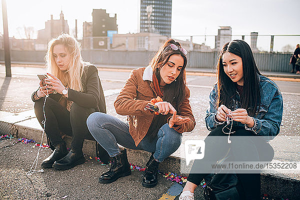 Freunde sitzen mit Smartphone am Bordstein  Mailand  Italien