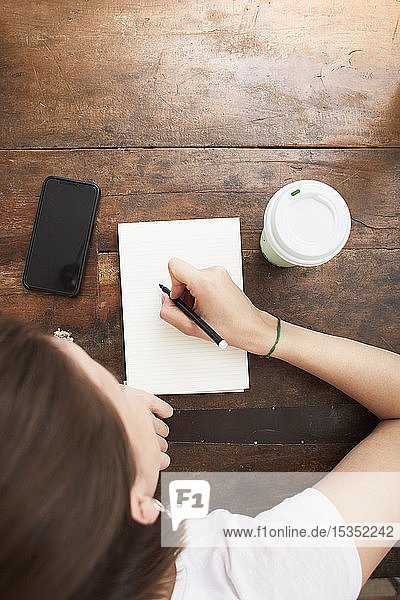 Frau schreibt in der Kaffeepause auf ein Notizbuch