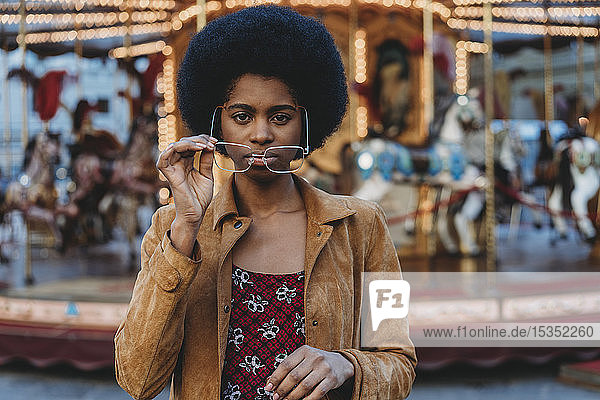 Junge Frau mit Afro-Haaren setzt vor dem Karussell eine Brille auf
