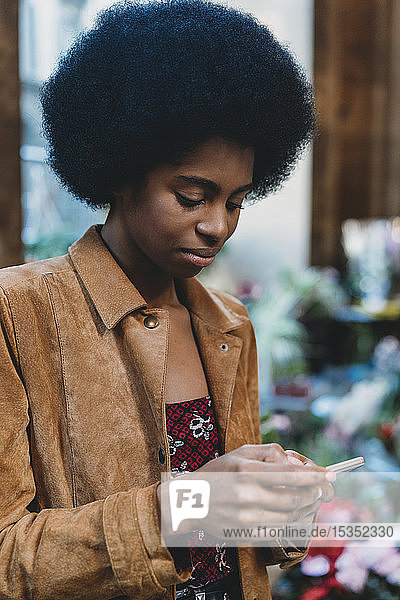 Young woman with afro hair using smartphone in city