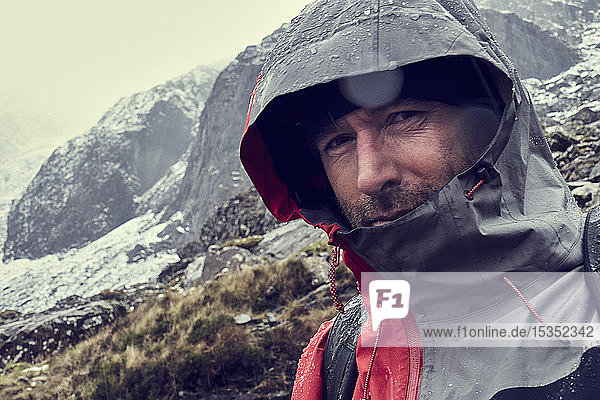 Male hiker with hood up in sleeting snow capped mountain landscape  close up portrait  Llanberis  Gwynedd  Wales