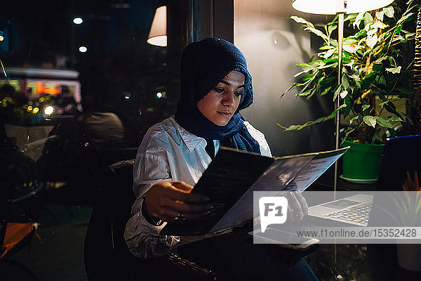 Junge Frau im Hijab betrachtet Speisekarte im Cafe