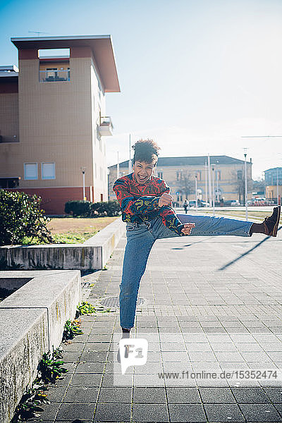 Junge Frau springt und tritt Bein auf städtischem Bürgersteig  Ganzkörperporträt