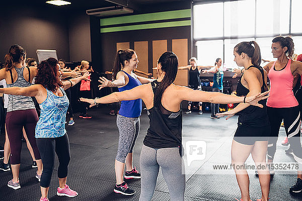 Gruppe von Frauen  die mit ausgestreckten Armen im Fitnessstudio trainieren