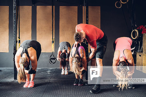 Frauen trainieren im Fitnessstudio mit männlichem Trainer  nach vorne gebeugt
