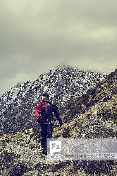 Männlicher Wanderer wandert in zerklüfteter Landschaft mit schneebedeckten Bergen  Llanberis  Gwynedd  Wales