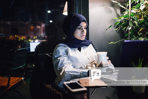 Junge Frau im Hijab betrachtet Laptop im Café