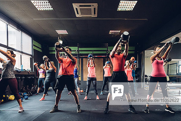 Frauen trainieren im Fitnessstudio mit männlichen Trainern und heben Kesselglocken