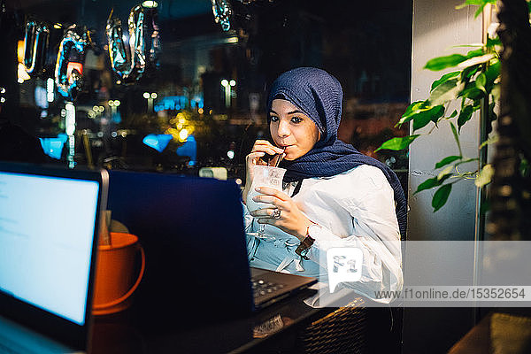 Junge Frau im Hijab trinkt Smoothie im Café