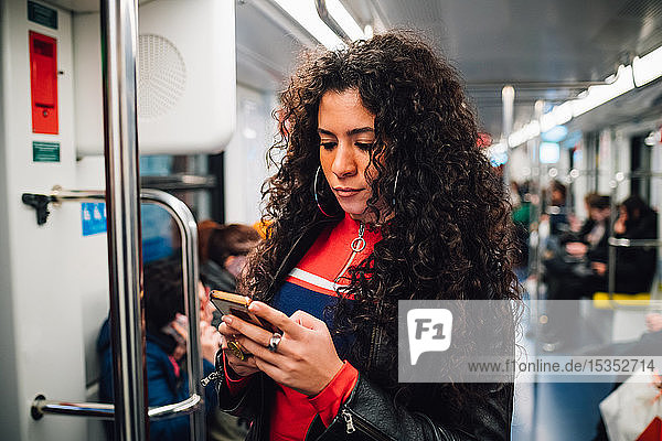 Mid adult woman with long curly hair looking at smartphone on city subway train
