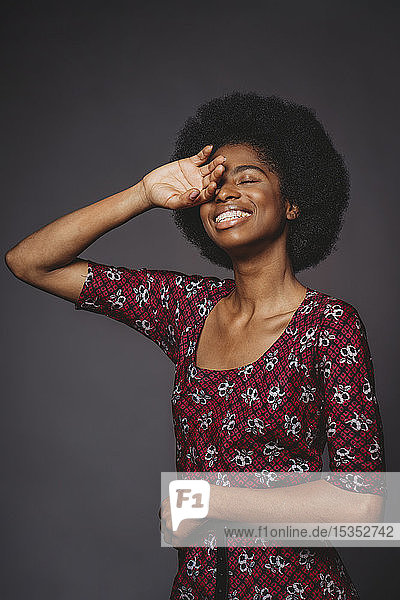 Junge Frau mit afrofarbenen Haaren  die das Auge bedecken  und lächelndem  grauem Hintergrund