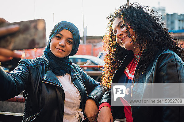 Young woman in hijab and friend posing for selfie in city