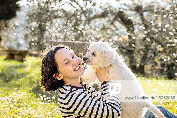 Girl sitting in orchard playing with a cute golden retriever puppy  Scandicci  Tuscany  Italy
