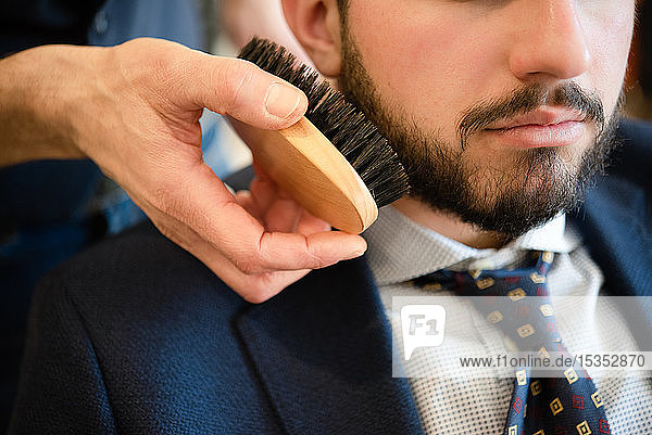 Hairdresser brushing customer's beard in barber shop