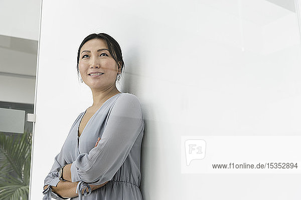 Businesswoman leaning against white wall in office