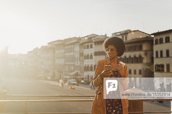 Junge Frau mit Afro-Haaren  die ein Heißgetränk zu sich nimmt und ein Smartphone benutzt  in der Stadt  Florenz  Toskana  Italien