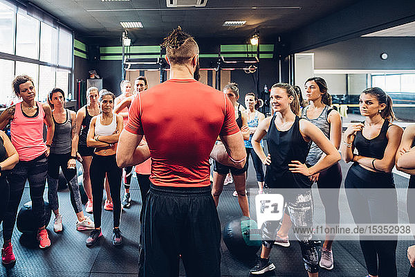 Gruppe von Frauen trainiert im Fitnessstudio  hört dem männlichen Trainer zu