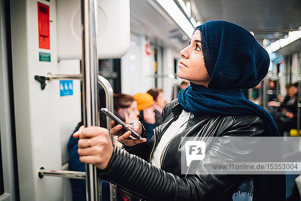 Junge Frau im Hijab mit Smartphone in der U-Bahn