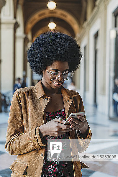 Junge Frau mit Afro-Haaren benutzt Smartphone im Gebäudekorridor